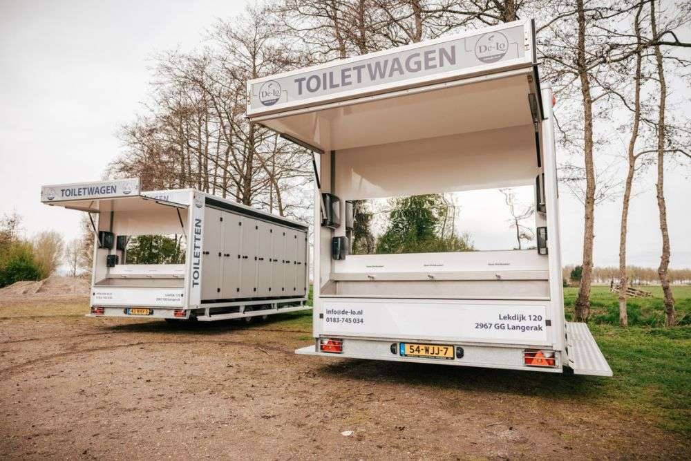Afbeelding van twee toiletwagens in een omgeving met bomen