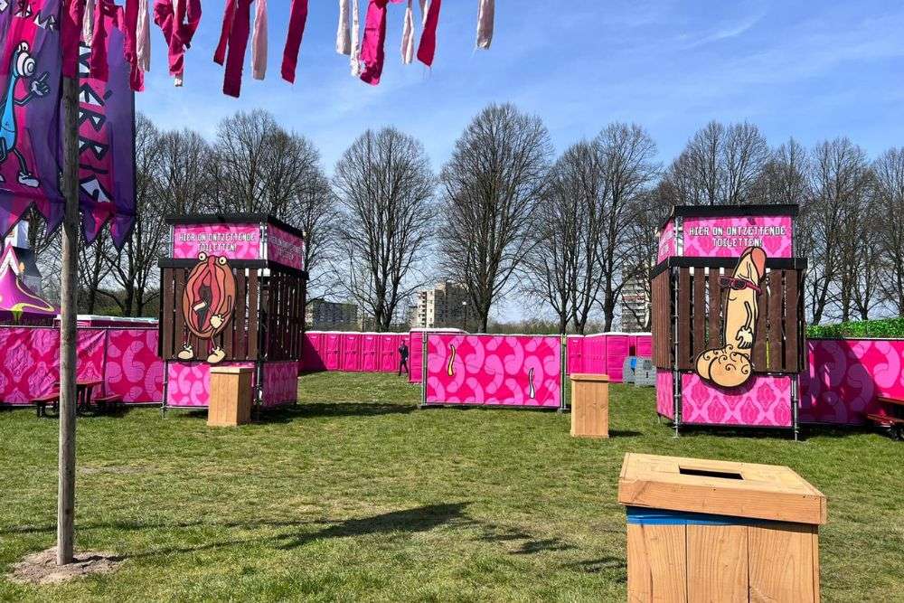 Festivalterrein met felroze toiletvoorzieningen en creatieve decoraties, waaronder humoristische illustraties op houten structuren, tijdens het Smerrig Festival 2023.
