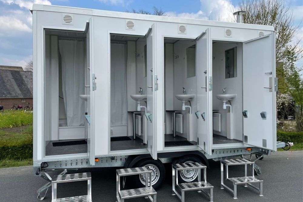 Mobiele douchewagen DL400 van De Lo met vier afzonderlijke cabines, elk uitgerust met een wastafel, spiegel en douchegedeelte.